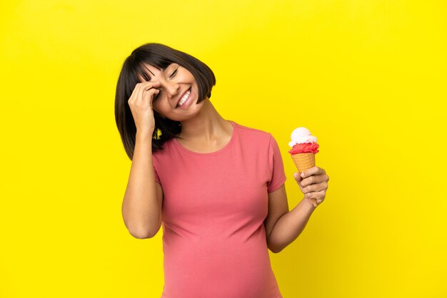 Pregnant woman holding a cornet ice cream isolated on yellow background smiling a lot