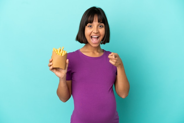 Pregnant woman holding fried chips over isolated background surprised and pointing front