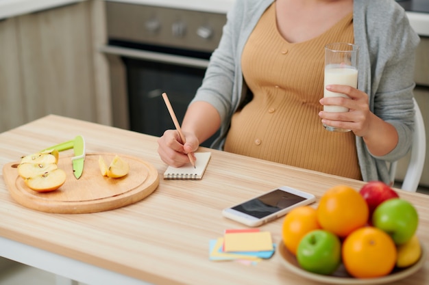 Pregnant woman holding glass milk expectant mother posing in kitchen