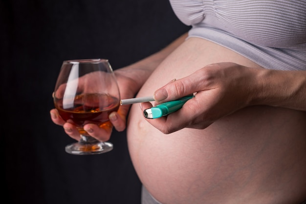 Pregnant woman holding a glass of whiskey and cigarette