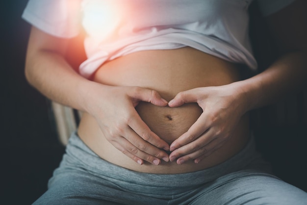 Pregnant woman holding hands in heart shape on belly at home.pregnant woman making heart with her hands, closeup.