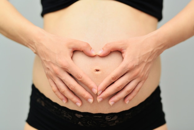 pregnant woman holding hands on her belly making a heart symbol