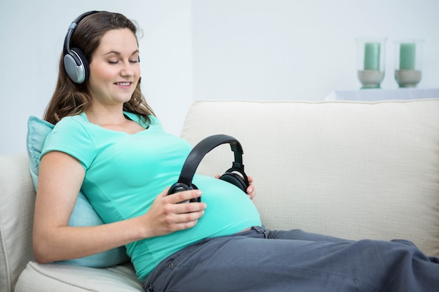 Pregnant woman holding headphone on belly on couch