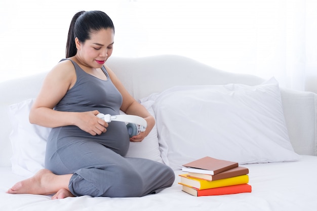 Pregnant woman holding headphones on belly.