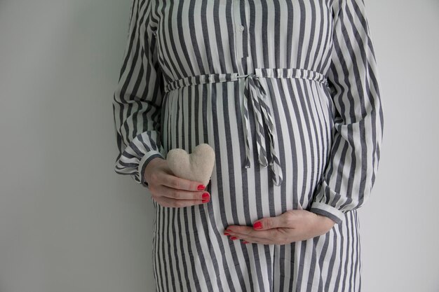 A pregnant woman holding a heart shape in front of here baby bump