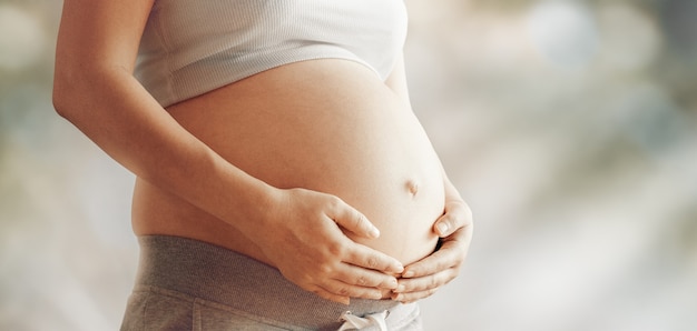 Pregnant woman holding her belly against nature bokeh background