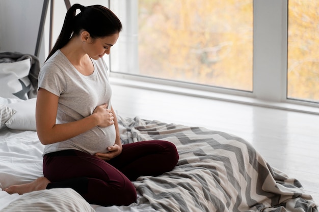 Photo pregnant woman holding her belly while sitting in bed with copy space