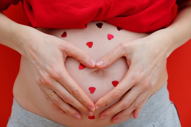 Pregnant Woman holding her hands in a heart shape on her baby bump. Pregnant Belly with fingers Heart symbol. Maternity concept. The concept of Valentine's day