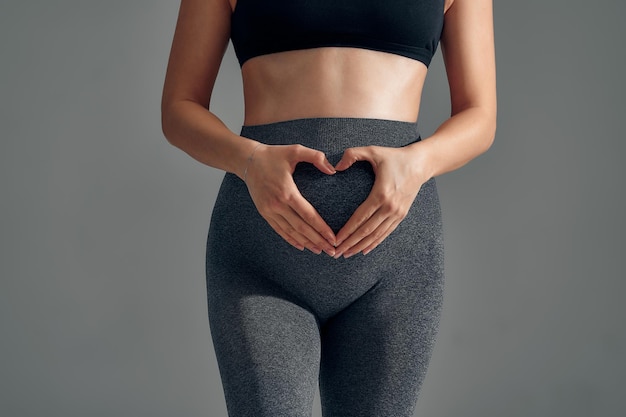 Donna incinta che tiene le sue mani a forma di cuore sulla sua pancia pancia incinta con il simbolo del cuore delle dita maternità maternità gravidanza concetto di felicità