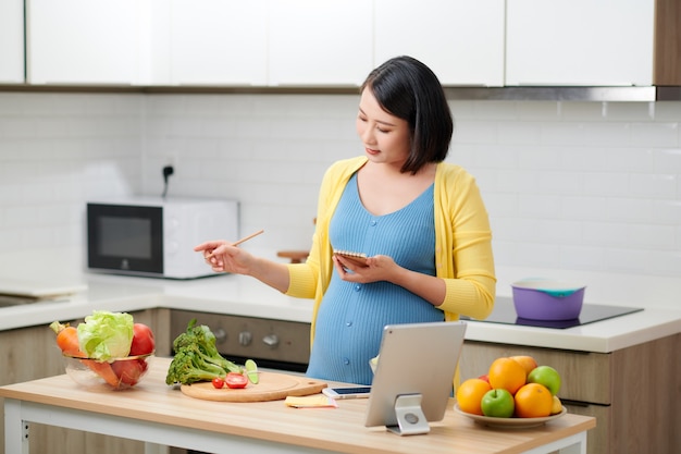 Pregnant woman holding a note-book and writing down the recipe