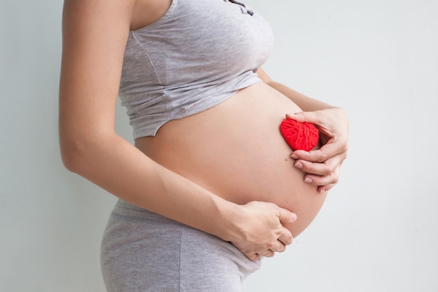 Photo pregnant woman holding red heart and hand on her belly, symbol of new life