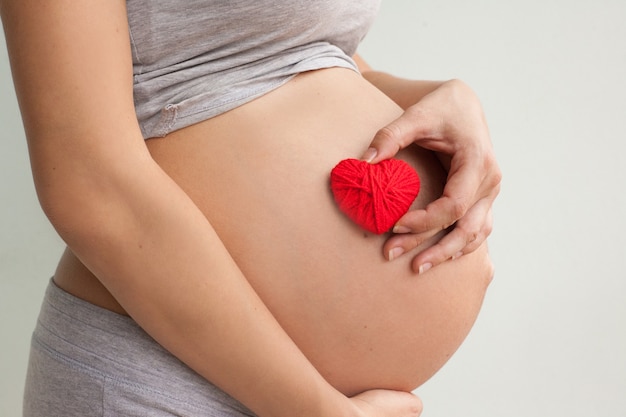 Pregnant woman holding red heart and hand on her belly, symbol of new life