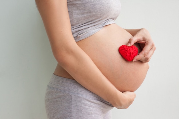 Pregnant woman holding red heart and hand on her belly, symbol of new life