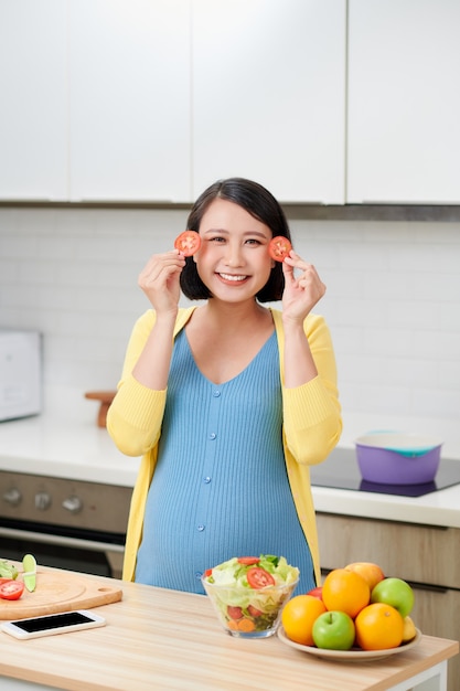 임신 한 여자는 슬라이스 토마토를 들고 임신 중 눈, 건강 식품 및 영양의 개념을 덮고