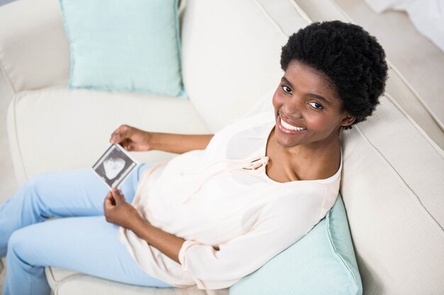 Pregnant woman holding ultrasound scan on couch