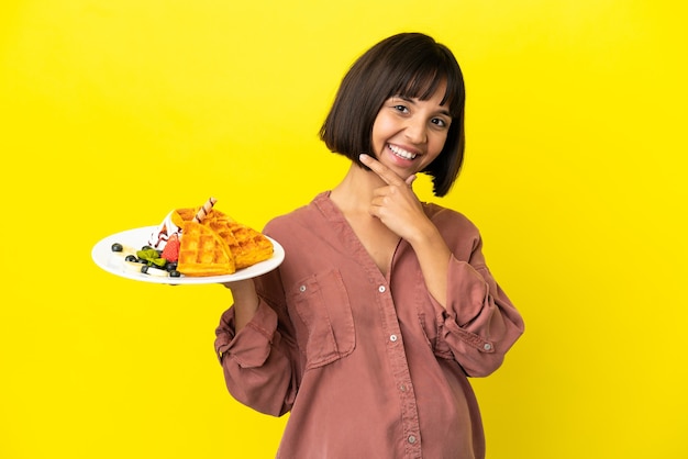 Фото Беременная женщина, держащая вафли, изолированные на желтом фоне, счастлива и улыбается