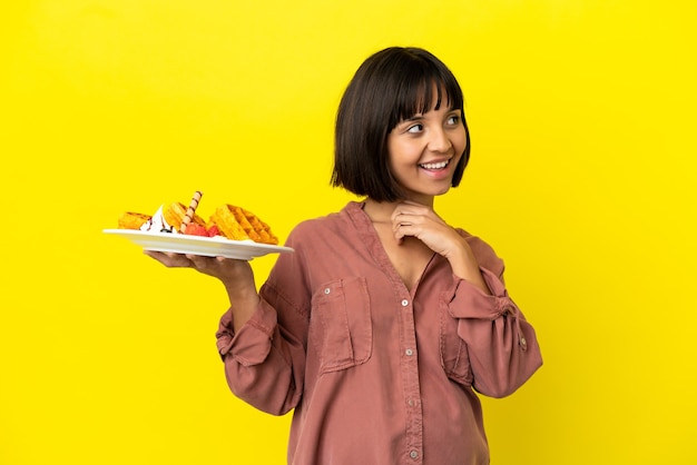 Pregnant woman holding waffles isolated on yellow background and looking up