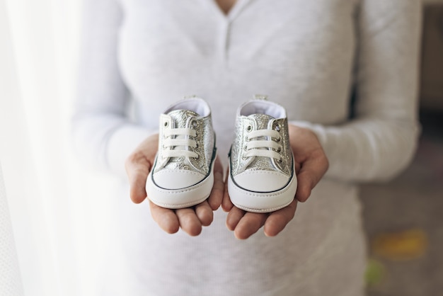 妊娠中の女性は、手に赤ちゃんのブーツ、クローズアップ、妊娠の概念、期待を保持します