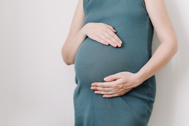 妊娠中の女性は白い背景の上の腹に手を保持します妊娠出産準備と期待の概念