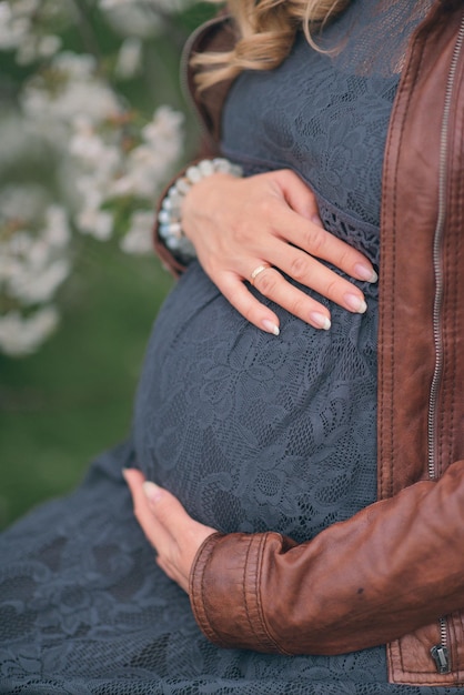 妊娠中の女性は、背景に花が咲く木の前でお腹を抱えています。