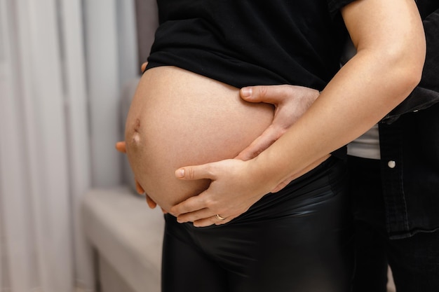 A pregnant woman holds her belly with her hand on her hip.