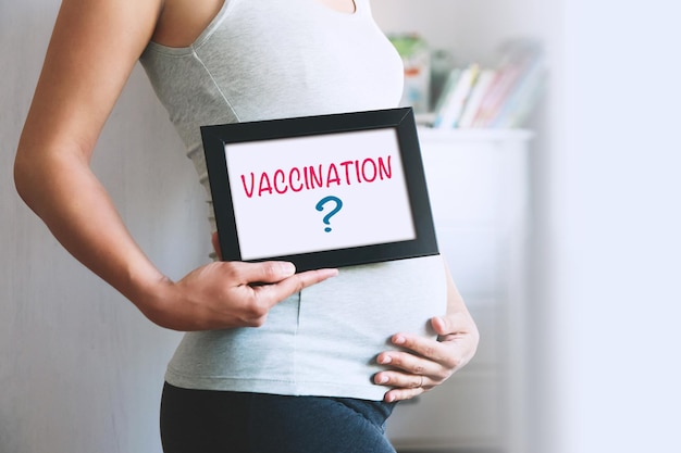 Pregnant woman holds whiteboard with text message  VACCINATION Pregnancy concept