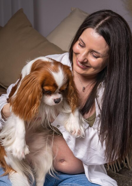 pregnant woman at home having fun playing with her dog Cavalier King Charles Cocker Spaniel