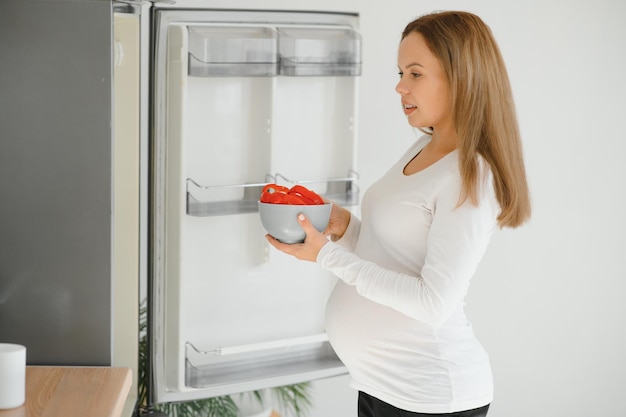 부엌에서 집에 있는 임산부가 냉장고를 엽니다