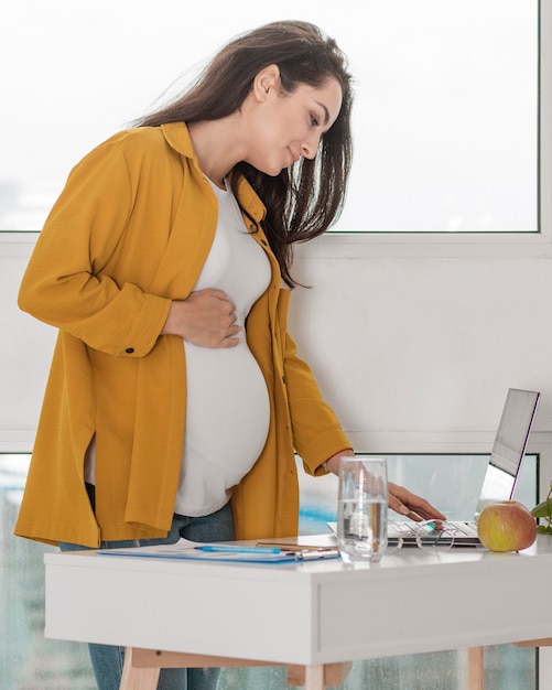 Беременная женщина дома работает на ноутбуке