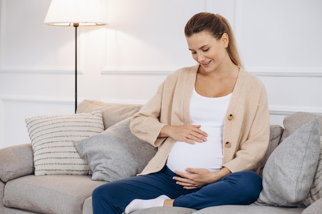 Pregnant woman hugging belly and sitting on sofa