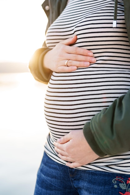 Pregnant woman hugs her belly closeup