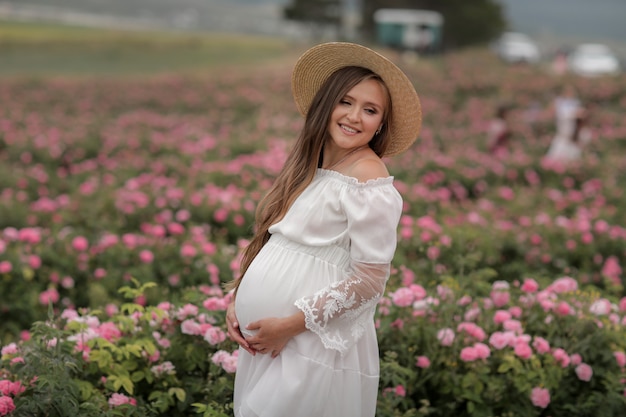 Фото Беременная женщина в соломенной шляпе на голове стоит в поле цветов