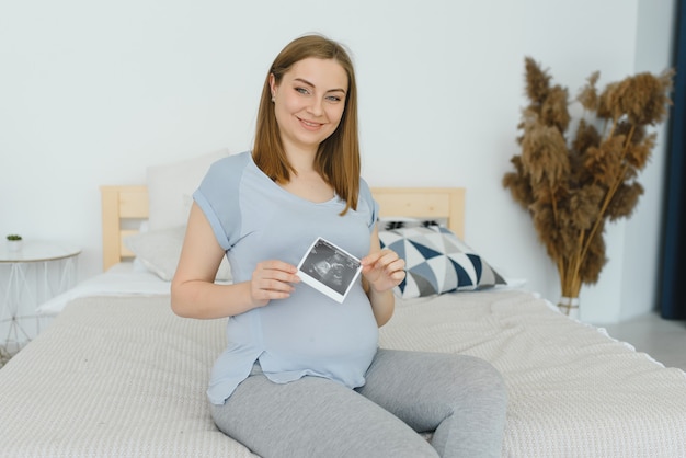 Pregnant woman is holding her stomach and a photo of her Ultrasound