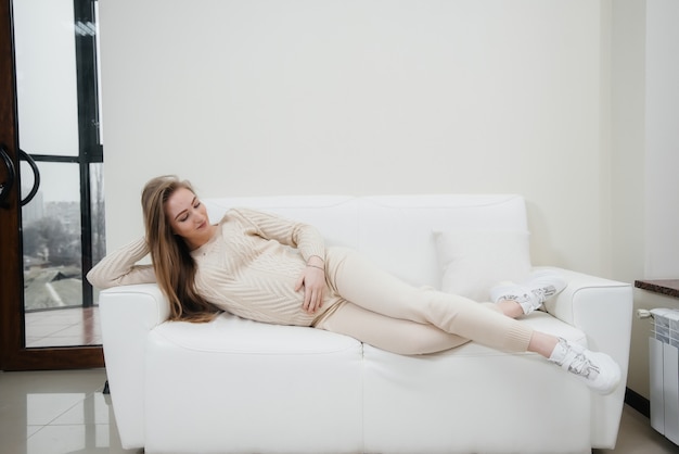 беременная женщина лежит на диване в гостиной и размахивая животом. Беременность и забота о будущем ребенка