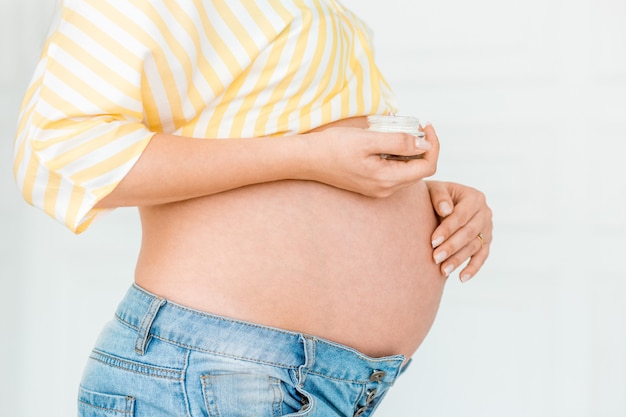 Pregnant woman is putting cream on her belly