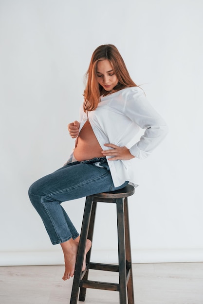 Pregnant woman is sitting on the chair in the studio
