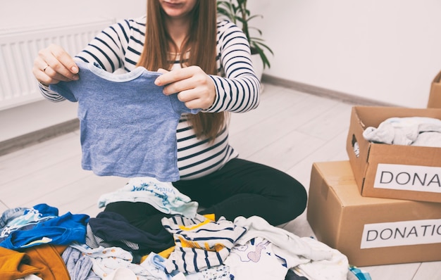 Беременная женщина разбирает детскую одежду и хочет отдать вещи на благотворительность