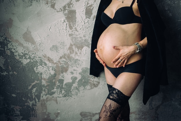 Беременная женщина стоит возле стены, обнимая живот