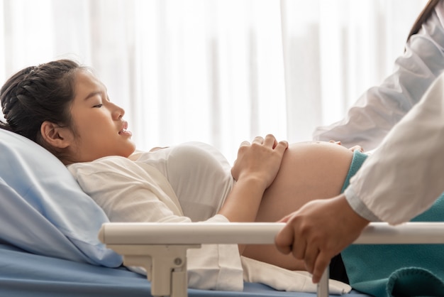 妊娠中の女性は苦しんでいるので、医師と一緒に患者のベッドに横たわっているので、産科と健康の概念に、分娩室にもたらすために、医師と一緒に患者のベッドに横たわっています。