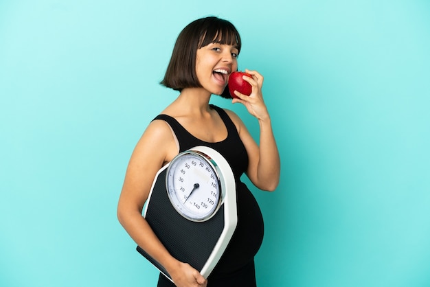 Pregnant woman over isolated background with weighing machine and with an apple