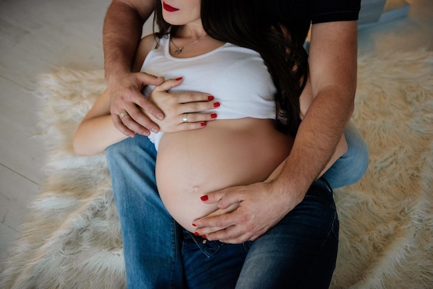 Pregnant woman in jeans and a white T-shirt. The husband hugs the belly.