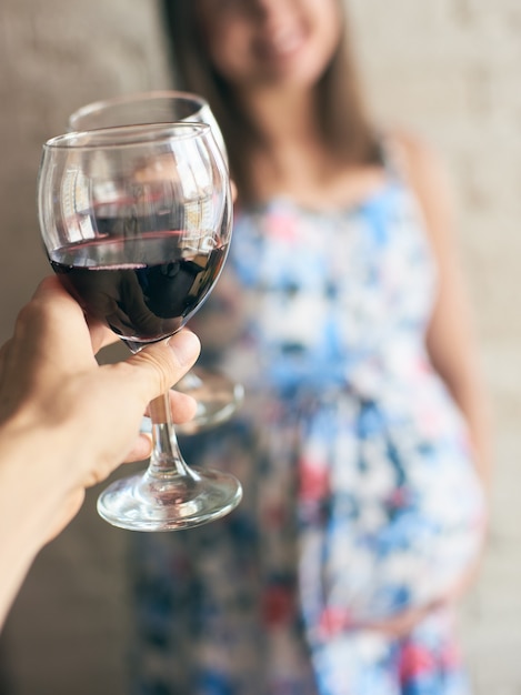 Беременная женщина держит бокал вина и аплодирует