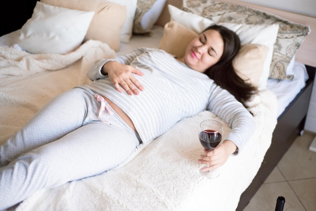 Pregnant woman keeping glass of wine Future mother drinking alcohol while expecting little baby Concept of unhealthy lifestyle and harmfulness