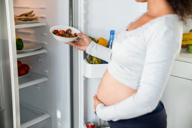 Pregnant woman keeping strawberries in fridge