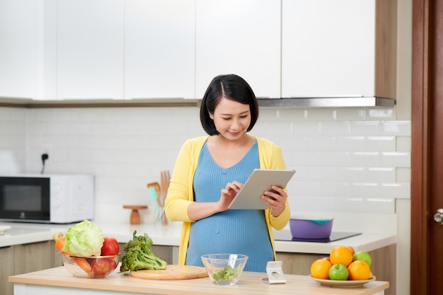 デジタルタブレットで健康的なサラダを作るキッチンの妊婦
