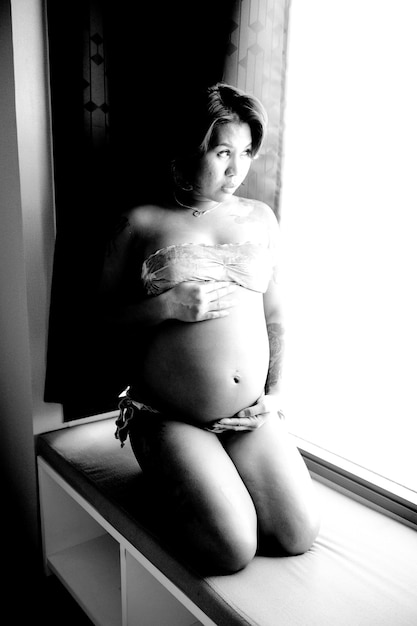 Photo pregnant woman kneeling by window at home