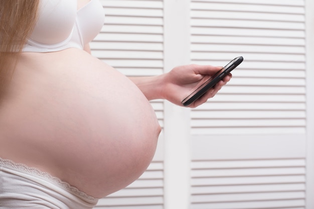 Pregnant woman in lingerie enjoys a smartphone. Call an ambulance. Prenatal contractions