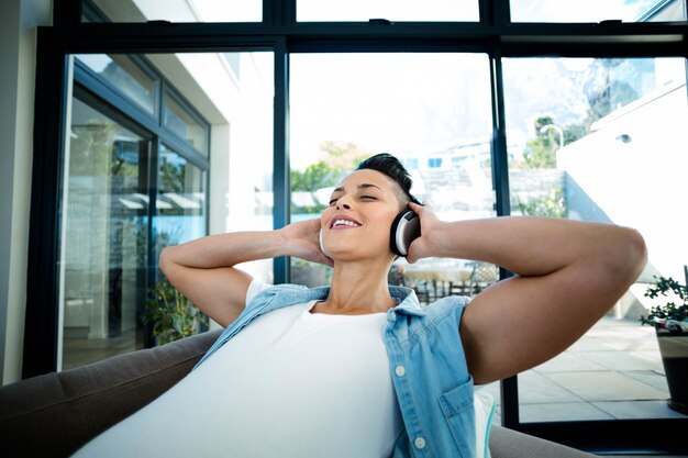 Pregnant woman listening to music on sofa in living room