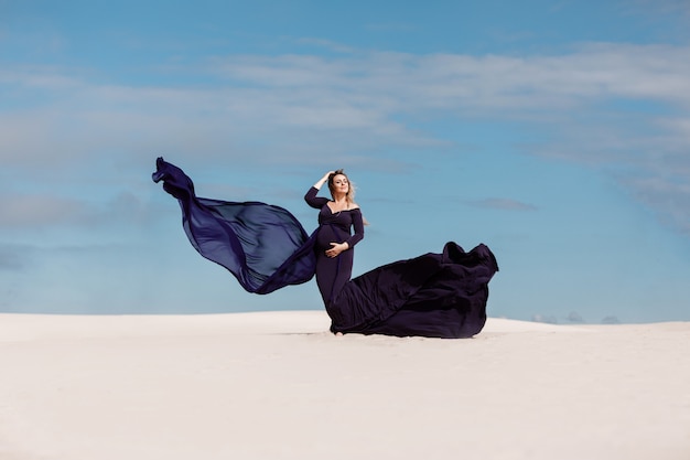 Foto donna incinta in un abito lungo nel deserto