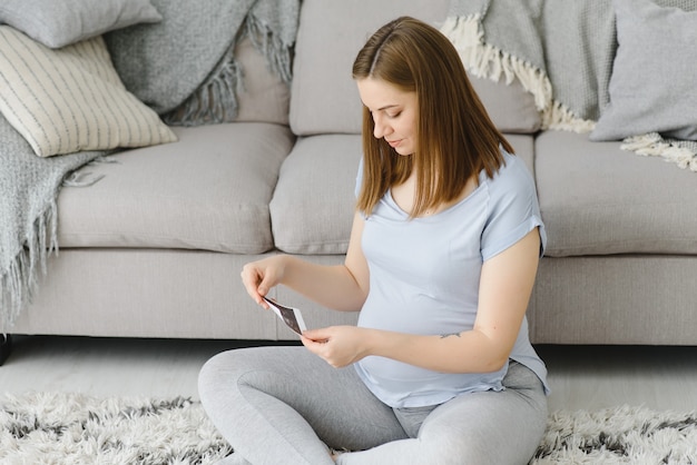 Pregnant woman looking at her baby sonography. Happy expectant lady enjoying first photo of her unborn child, anticipating her future life, copy space